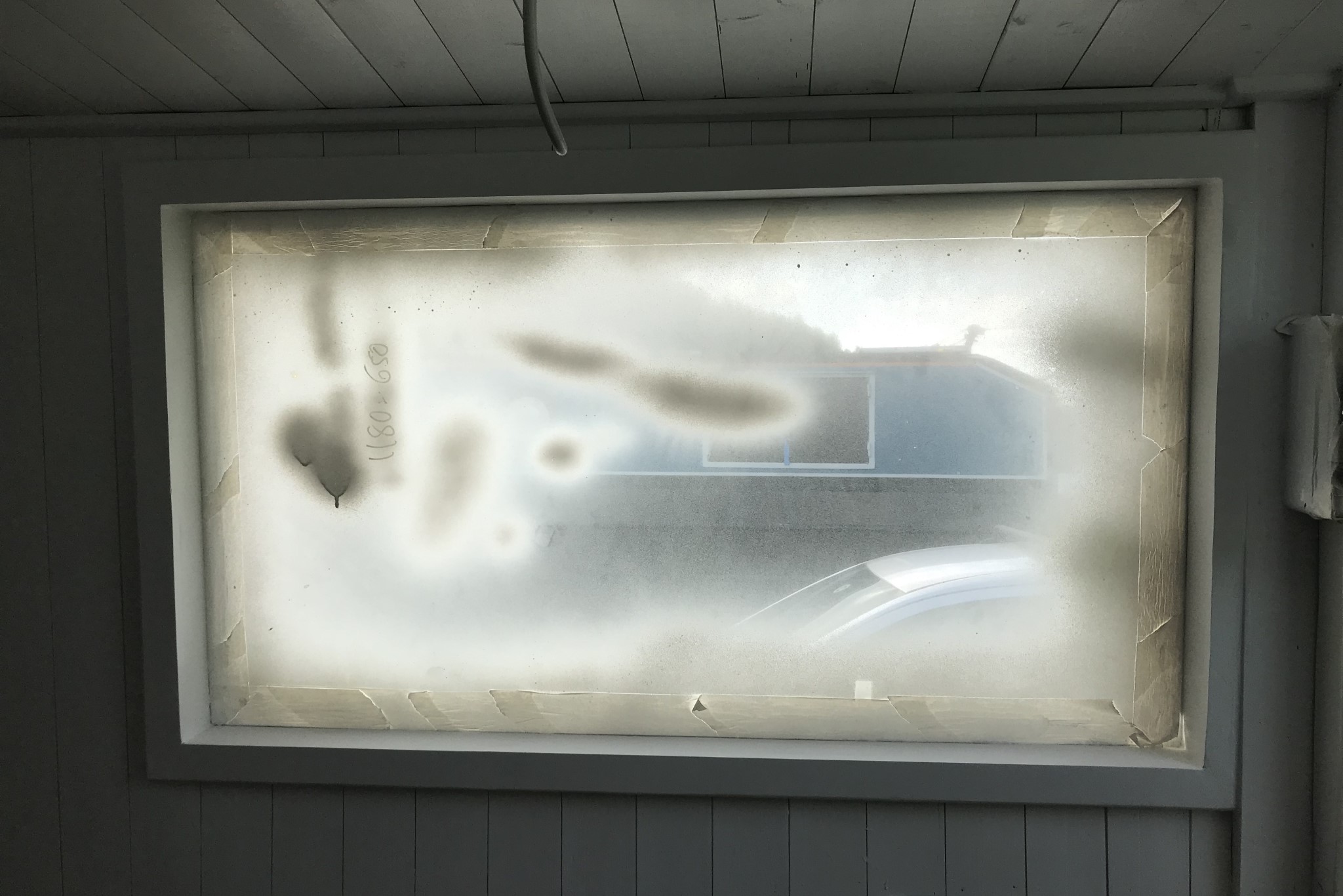 A window in the boat with protective tape around the edges to protect it from paint. The paint is all over the window and the tape has done nothing to protect it.